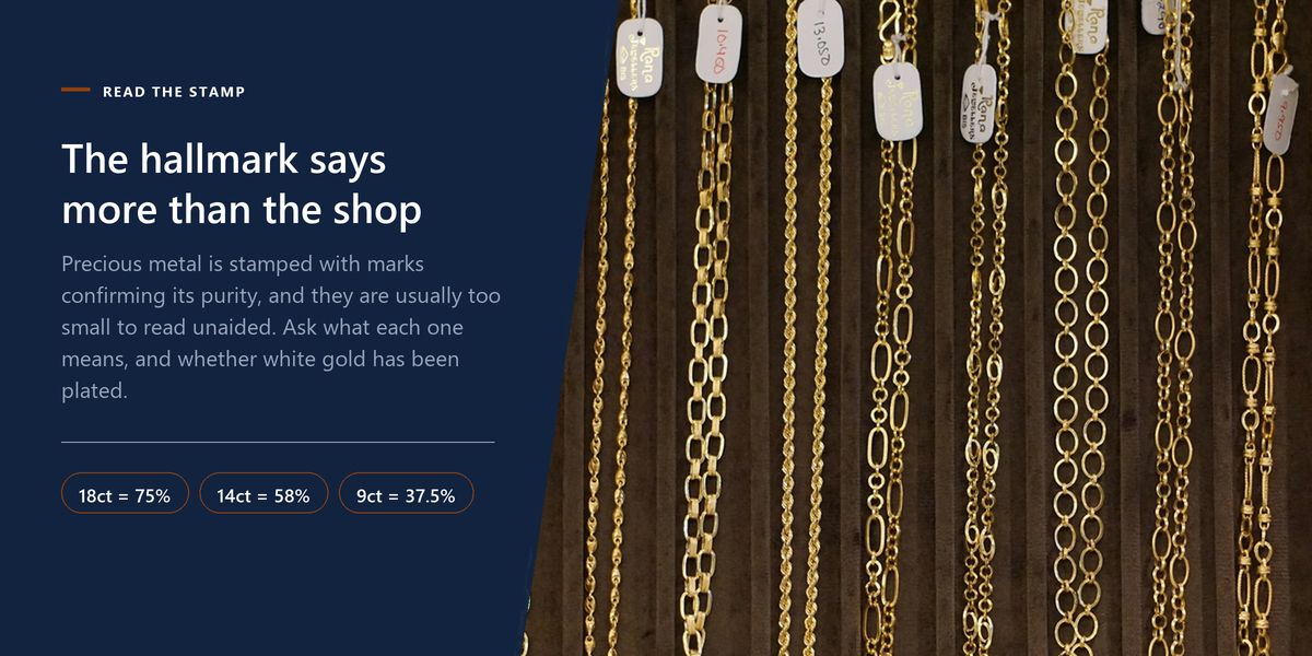 Rows of gold chains hanging with small paper tags on a jeweller's display board, beside a panel on reading hallmarks and carat marks.